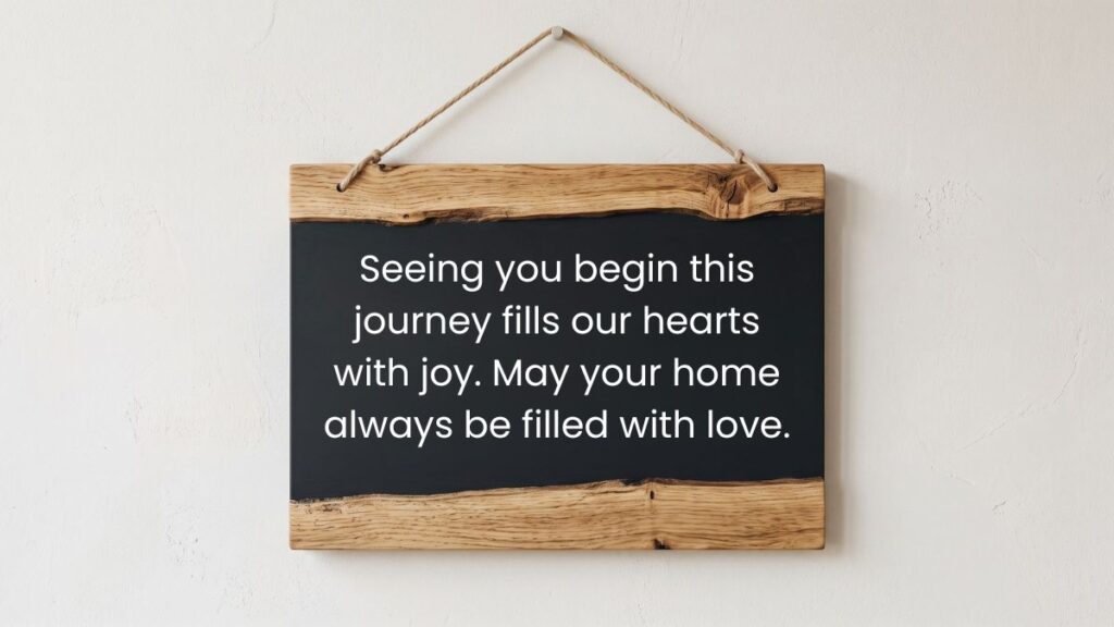 Hanging wooden chalkboard sign displaying joyful wedding wishes against a plain white wall background.